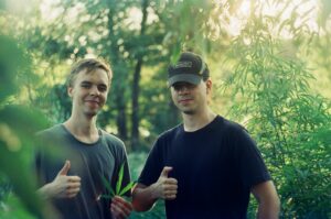 two men standing next to each other in a forest